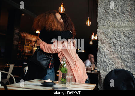 Two young women meeting at a restaurant. Friends hugging each other at a cafe. Stock Photo