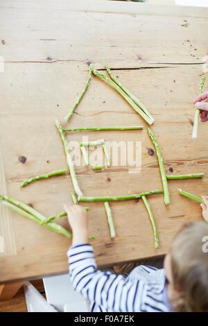 Boy playing with asparagus on dining table Stock Photo