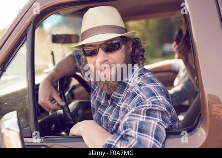 Mid adult man leaning out of vehicle window wearing sunglasses and hat Stock Photo