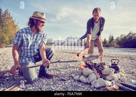 Adult men cooking fish attached to branch over campfire, Wallgau, Bavaria, Germany Stock Photo