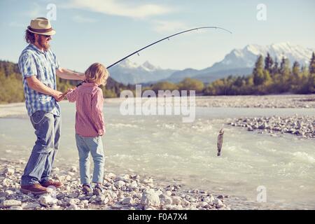 Mid adult man and boy near river holding fishing rod with fish attached, Wallgau, Bavaria, Germany Stock Photo