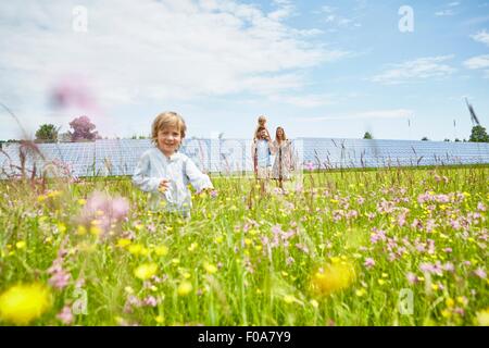 Young boy running through field, mother, father and brother following behind, next to solar farm Stock Photo