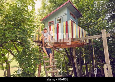 Young couple sitting on ladder of tree house Stock Photo