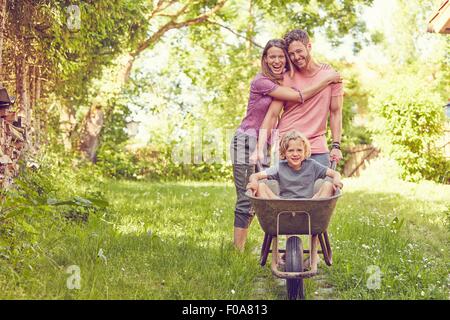 Portrait of young family, father pushing son in wheelbarrow Stock Photo