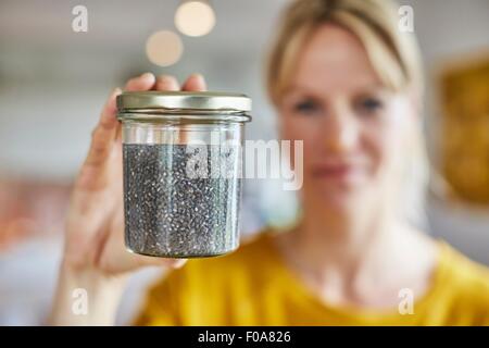 Mature woman holding up jar of seeds, focus on seeds Stock Photo
