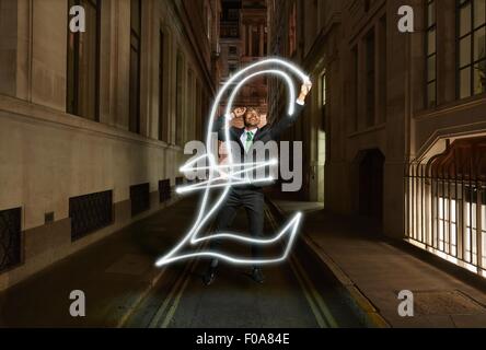 Young businessman light painting pound sterling symbol on city street at night, London, UK Stock Photo