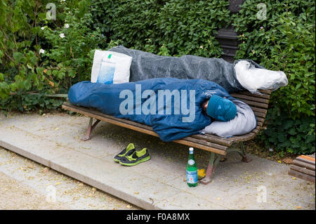 PARIS, FRANCE - JULY 27, 2015: A homeless man is sleeping on a bench in a park in Paris in France Stock Photo