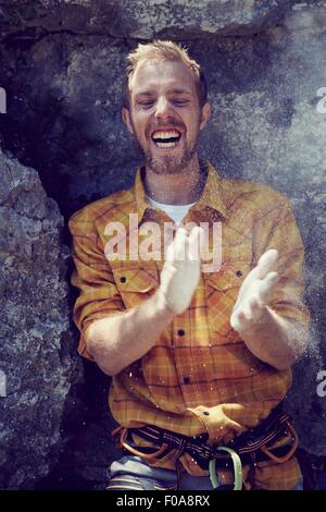 Climber leaning against rock wall clapping chalked hands, Ehrwald, Tyrol, Austria Stock Photo