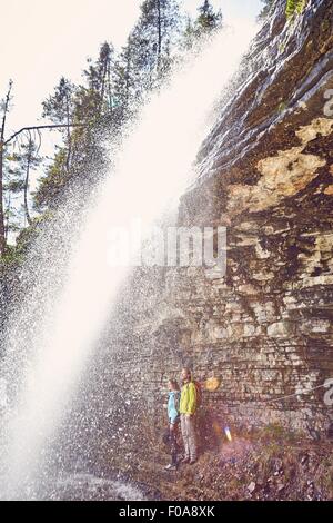 Young couple standing underneath waterfall, looking out,  Tyrol, Austria Stock Photo