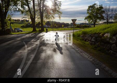 Rear silhouetted view of boy cycling on rural road Stock Photo