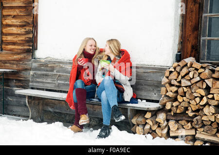 Two young female friends drinking coffee outside wooden cabin Stock Photo