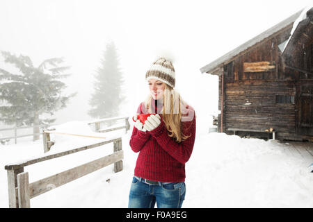 Young woman drinking coffee in snow outside cabin Stock Photo