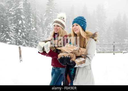 Two young female friends carrying logs in snowy mist Stock Photo