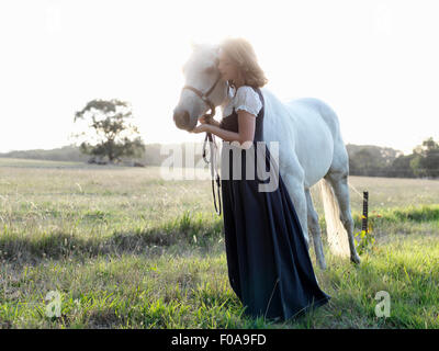 Portrait of teenage girl with grey horse in sunlit field Stock Photo