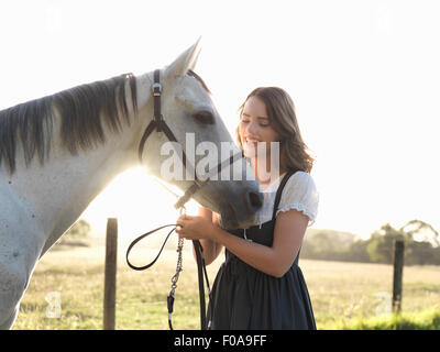 Portrait of teenage girl and her grey horse in sunlit field Stock Photo
