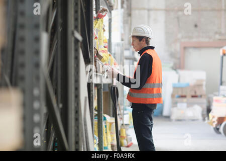 Young male warehouse worker searching shelves with clipboard in warehouse Stock Photo