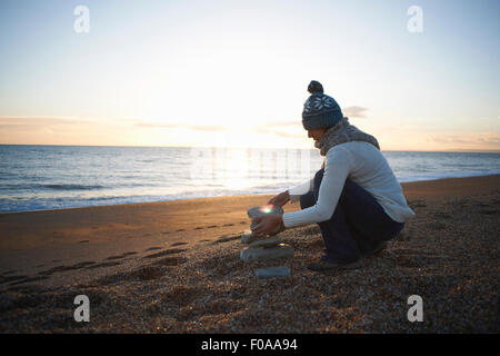 Mature woman stacking stones on beach at dusk Stock Photo