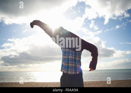 Mature man struggling to put on sweater at beach Stock Photo