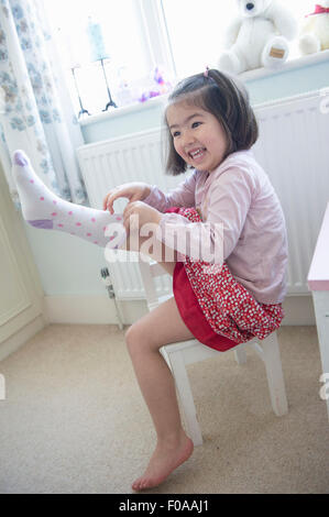 Young girl sitting on chair, pulling sock on Stock Photo