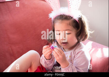 Young girl wearing bunny ears, looking at fluffy Easter chick Stock Photo