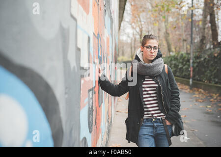 Teenager leaning against graffiti wall Stock Photo