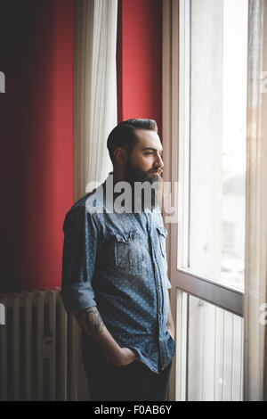 Young bearded man standing by window Stock Photo