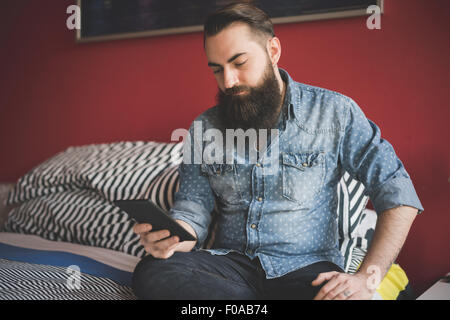 Young bearded man using smartphone on bed Stock Photo