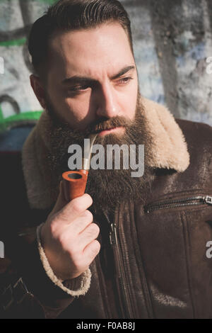 Young bearded man smoking pipe by graffiti wall Stock Photo