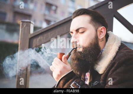 Young bearded man smoking pipe on steps Stock Photo