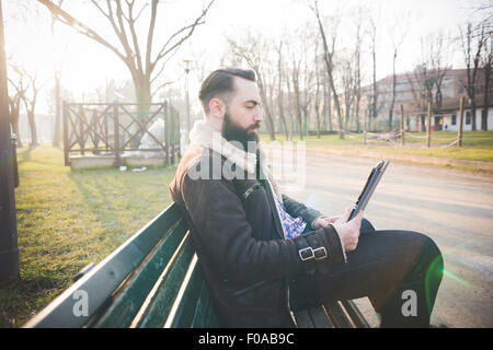 Young bearded man using digital tablet on park bench Stock Photo