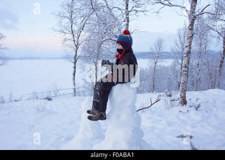 Boy sitting on top of snow man, Hemavan,Sweden Stock Photo