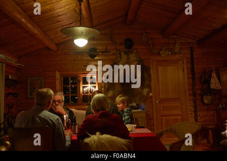 Three generation family sitting talking at Christmas table in log cabin at night Stock Photo