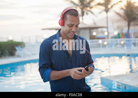 Mid adult man selecting smartphone music at hotel poolside, Rio De Janeiro, Brazil Stock Photo