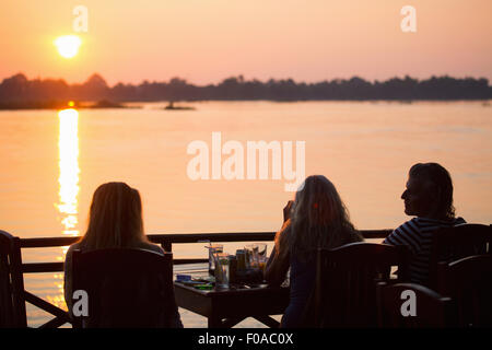 Rear view of three adult friends watching sunset over Mekong River, Don Det, Laos Stock Photo