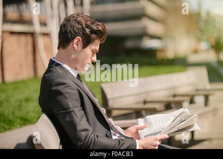 Young city businessman sitting on bench reading newspaper Stock Photo