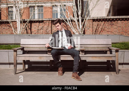 Young city businessman reading newspaper on bench Stock Photo