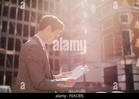 Young city businessman reading newspaper whilst walking Stock Photo