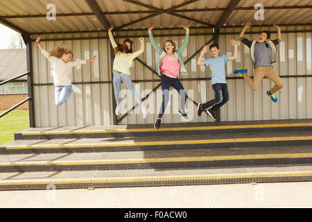 Five boys and girls jumping mid air in stadium stand Stock Photo