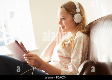 Girl on sofa wearing headphones listening to music from digital tablet
