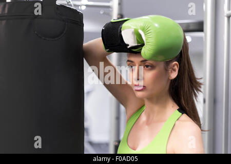 Portrait of a young woman at gym leaning against punchbag wearing boxing glove Stock Photo