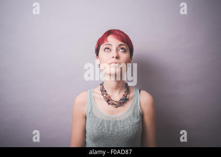 Studio portrait of young woman with short pink hair looking up