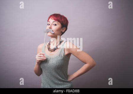 Studio portrait of young woman holding up mustache in front of face Stock Photo