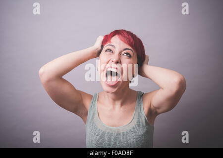 Studio portrait of young woman with hands in hair shouting Stock Photo