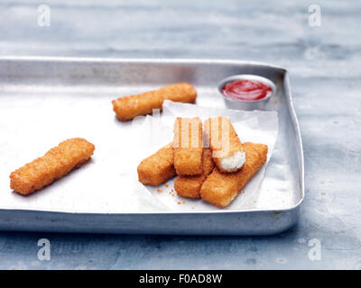 Baking tin with fried chunky cod breaded fish fingers with tomato ketchup Stock Photo