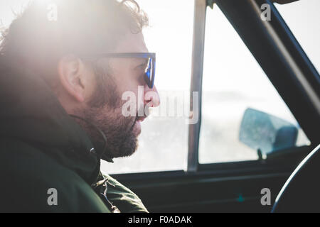 Close up of mid adult man wearing sunglasses in sunlit car Stock Photo