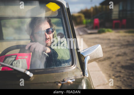 Man in parked vintage car looking through wing mirror Stock Photo