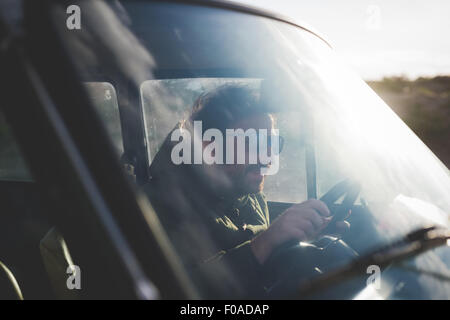 Man wearing sunglasses driving car in sunlight Stock Photo