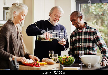 Senior man pouring wine in kitchen, woman preparing food Stock Photo