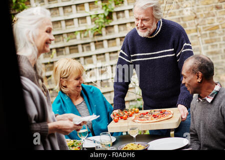 Senior man serving friends pizza in garden Stock Photo