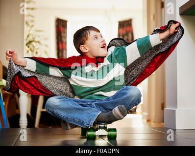 Young boy sitting on skateboard wearing cape Stock Photo